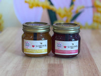 Two jars of Slabtown preserves on a wooden surface with a blurred floral background.